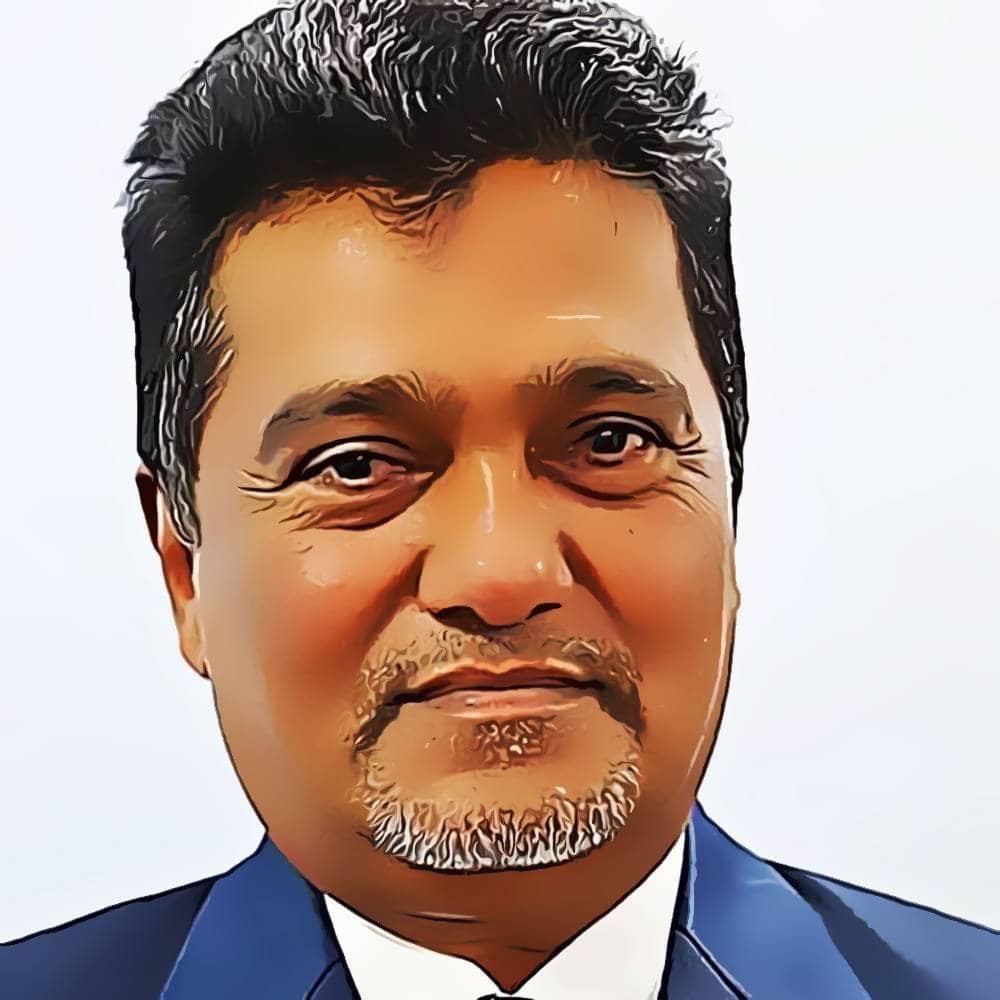 Portrait of a middle-aged man in a suit and tie with dark hair and a trimmed beard, representing expertise in Ayurvedic wellness and Panchakarma.