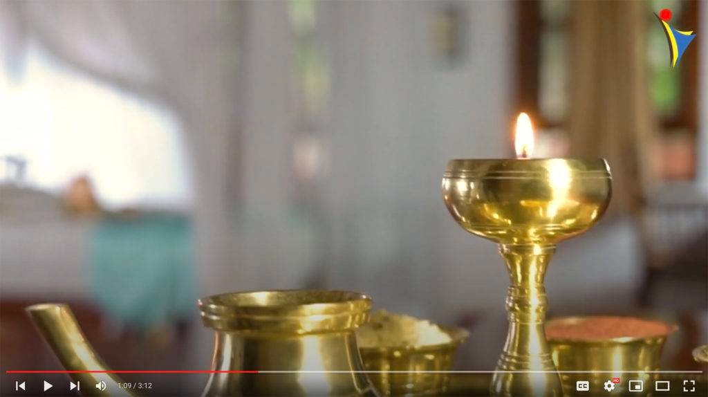 Brass oil lamp with a lit flame at IVAC Ayurvedic Centre, India, set against a blurred interior, showcasing traditional Ayurvedic ambiance.