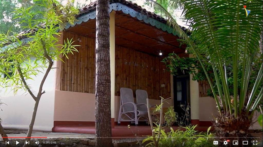 Traditional Ayurvedic accommodation with bamboo walls and wooden furniture surrounded by lush greenery at IVAC Ayurvedic Centre, India.