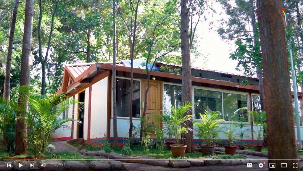 Scenic view of an eco-friendly, modern cabin surrounded by lush greenery at IVAC Ayurvedic Centre in India. Tranquil forest setting with tall trees and potted plants enhancing the natural ambience.