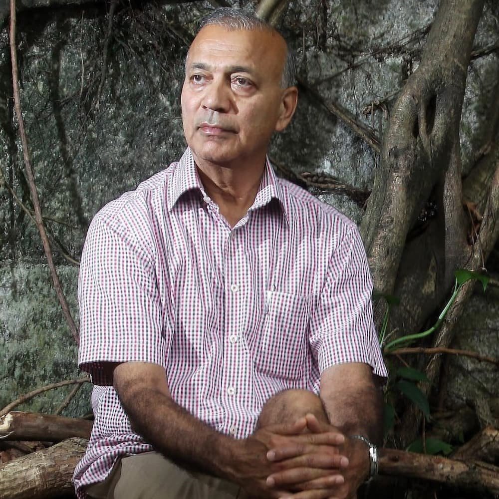 Portrait of an elder man in a checkered shirt sitting outdoors, surrounded by nature, embodying Ayurvedic wellness and Panchakarma expertise.