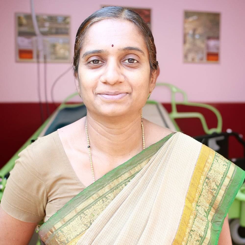 Woman in traditional Indian saree smiling, background shows an Ayurvedic wellness clinic with Panchakarma treatment equipment.
