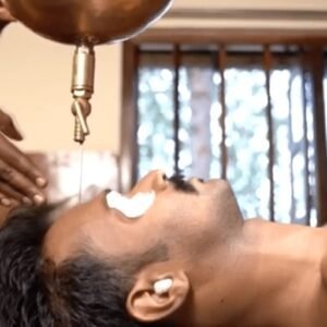 Close-up of a traditional Ayurvedic Shirodhara therapy, where a steady stream of warm oil is poured onto a patient's forehead to promote relaxation and mental clarity.