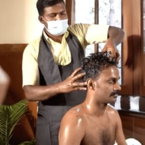 A therapist at IVAC performing a traditional Ayurvedic head massage on a guest, showcasing the holistic care approach. The guest, seated comfortably, receives the therapeutic touch that promotes relaxation, scalp nourishment, and mental clarity, set against a backdrop of natural light streaming through wooden windows, emphasizing IVAC’s serene and nurturing environment.